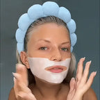 Woman with blue padded headband applying Lakerain® Bio-Collagen Deep Hydration hydrogel mask under chin against grey background