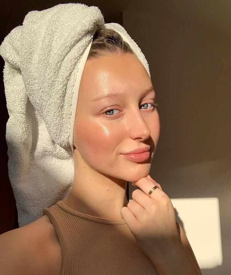 Young woman with glowing hydrated skin wearing a white towel wrapped around her head, showcasing natural beauty